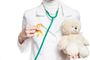 Doctor holding a gold cancer ribbon and teddy bear
