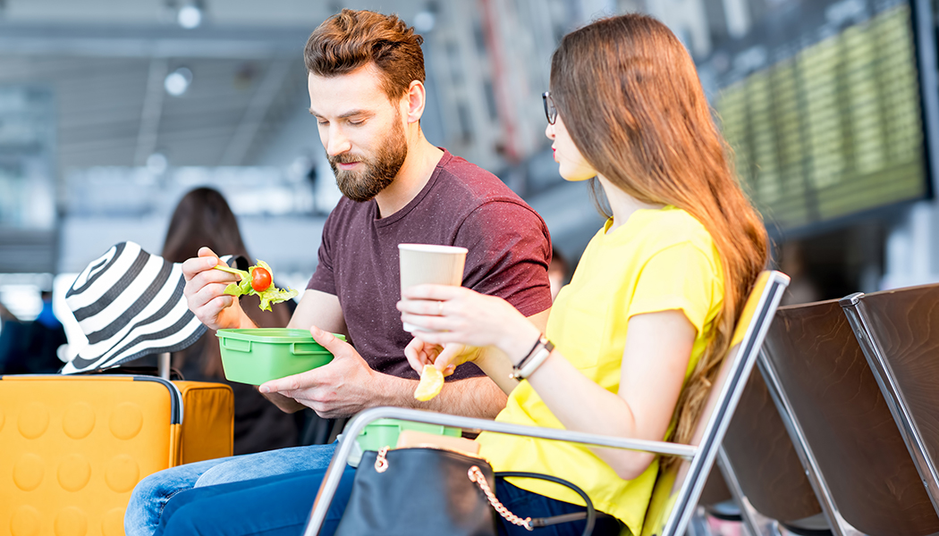Young,Couple,Having,A,Snack,With,Lunch,Boxes,At,The Young couple having a snack with lunch boxes at the waiting hall of the airport during their vacation